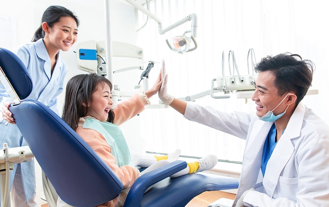 Dentist high fiving a kid in dentist chair with dental assistant watching